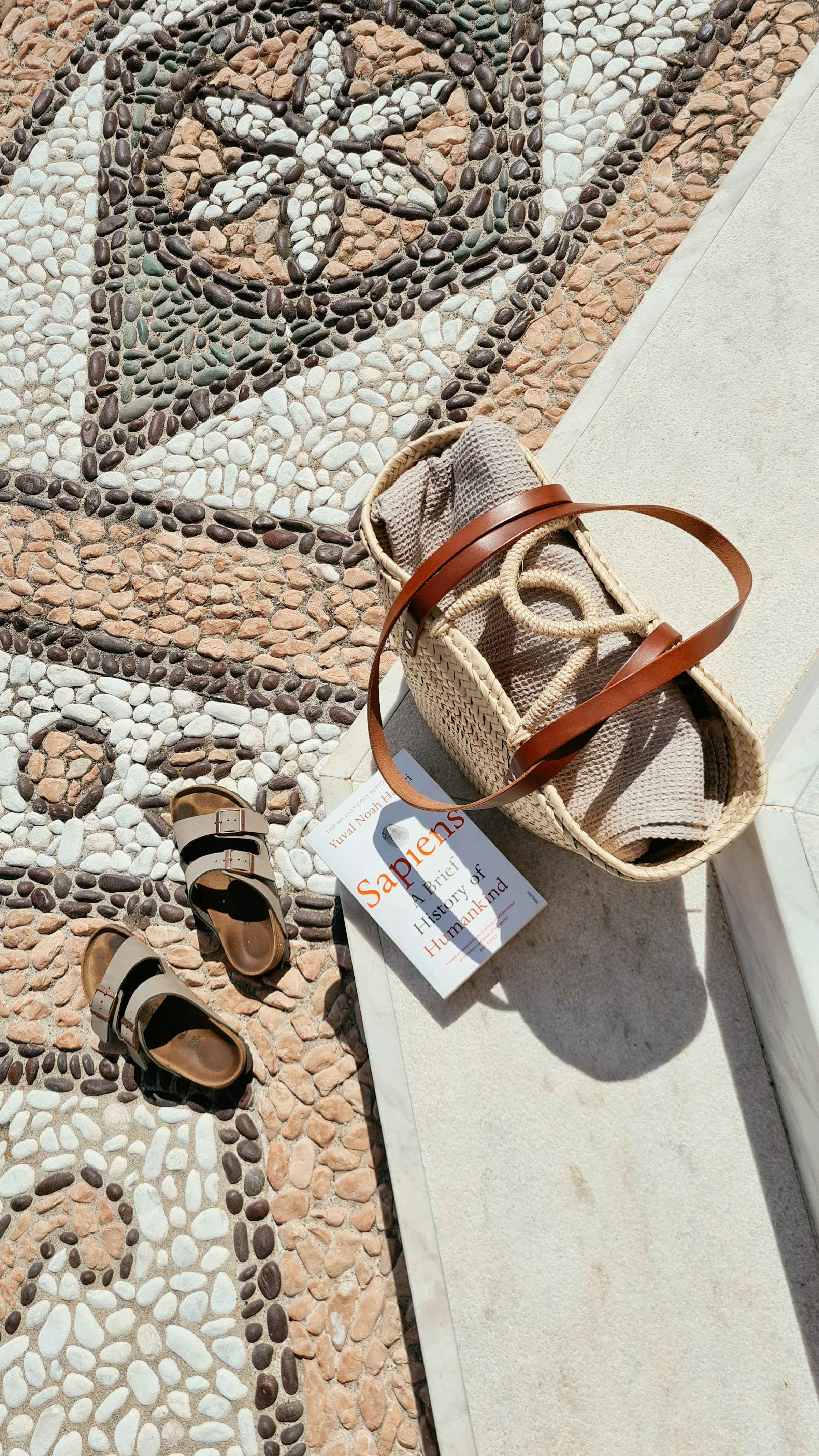 Neutral leather sandals arranged beside a woven beach bag